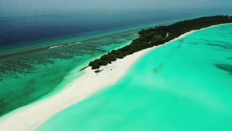Long-tropical-island-with-dense-green-plants-and-wide-white-sandy-beach-located-in-the-middle-of-turquoise-lagoon-and-coral-reef-barrier-in-Dhigurah,-Maldives