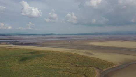 Aerial-shot-over-a-coastal-bay-when-the-tide-is-out,-showing-flat-golden-sand,-bright-sunny-day