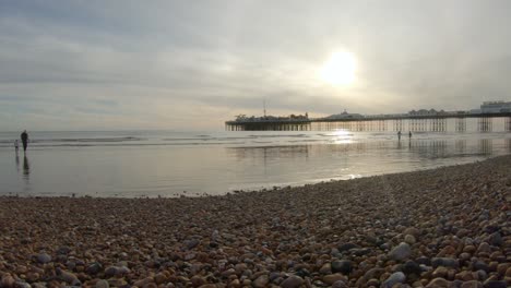 Brighton-beach-with-sun-setting-over-the-pier-and-people-walking-through-the-waves