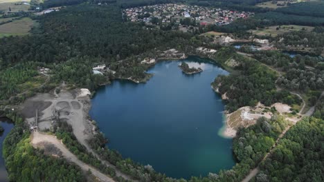 Aerial-View-of-lake-with-Beautiful-Water-in-a-Quarry-Surrounded-by-Forest,-Small-Town-and-Mining-Operation