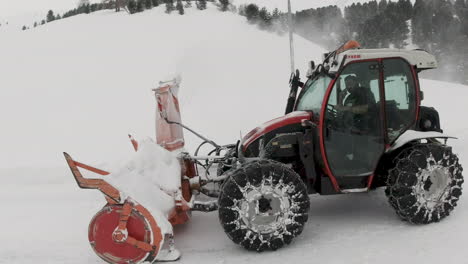 Man-on-phone-driving-tractor-clearing---blowing-heavy-snowfall-from-snow-covered-mountain.