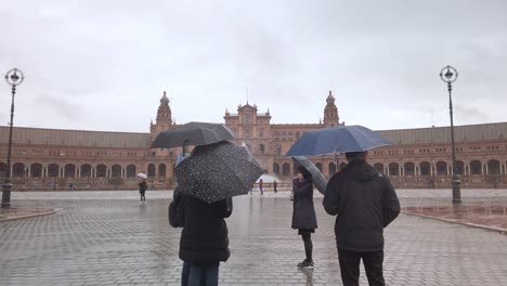 Bewegung-Auf-Touristen-Mit-Sonnenschirmen-Auf-Der-Verregneten-Plaza-De-Espana,-Sevilla,-Slowmo