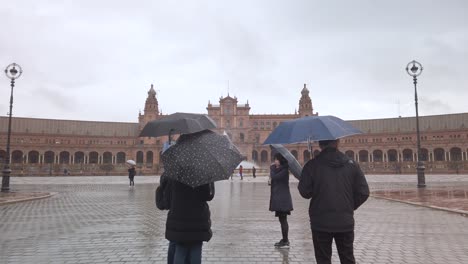 Moviéndose-Hacia-Los-Turistas-Con-Sombrillas-En-La-Lluviosa-Plaza-De-España,-Sevilla,-Cámara-Lenta