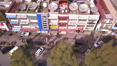 Aerial-view-of-drone-flying-over-a-busy-town-village-in-Asia-with-the-view-of-shops,-cars,-motorcycles,-pine-trees-and-famous-monument
