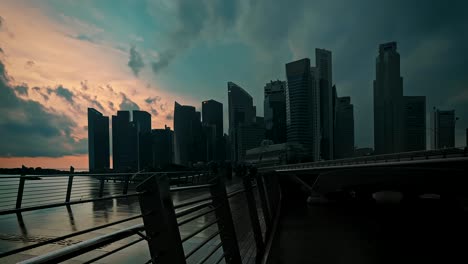Lapso-De-Tiempo-Que-Muestra-A-Los-Peatones-Cruzando-El-Puente-Del-Jubileo-En-Un-Clima-Lluvioso-Con-El-Horizonte-De-La-Ciudad-De-Singapur-En-El-Fondo