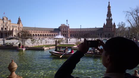Silhouette-Asiatischer-Mann-Fotografiert-Boote-Im-Plaza-De-Espana-Kanal,-Sevilla