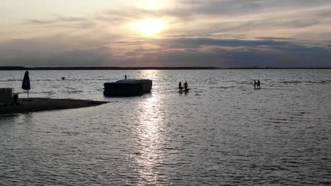 Luftaufnahme-Von-Menschen-Und-Schlauchbooten-Am-Flussufer-In-Silhouette-Bei-Sonnenuntergang