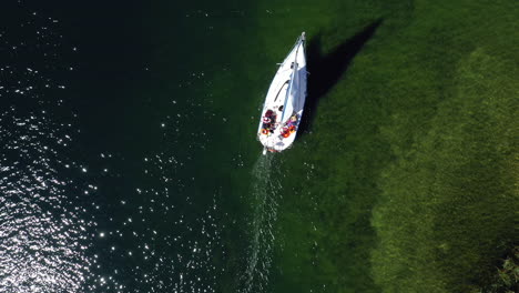 AERIAL:-Top-Down-or-Birds-Eye-View-of-White-Yacht-With-Group-of-People-Sailing-Near-the-Shallow-Part-of-the-Trakai-Lake