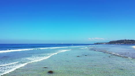 White-waves-washing-rocky-sea-bottom-on-shore-of-tropical-island,-beautiful-seascape-with-blue-sea-and-sky-on-a-bright-morning-in-Indonesia