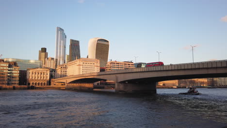 Double-decker-British-red-bus-driving-over-a-bridge-towards-corporate-office-skyscrapers