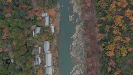 Drone-view-over-train-line-and-Japanese-river-in-autumn-season,-Arashiyama,-Kyoto