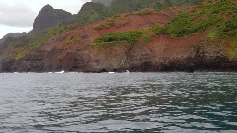 HD-120fps-Hawaii-Kauai-Bootfahren-Auf-Dem-Ozean,-Schwenk-Von-Rechts-Nach-Links-Von-Der-Felsigen-Küste-Vorbei-An-Kleinen-Wasserfällen-Bis-Zu-Den-Klippen-In-Der-Ferne