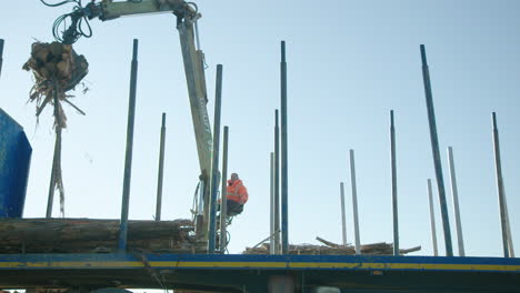 Worker-operators-crane-with-claw-to-stack-lumber-on-truck,-low-angle