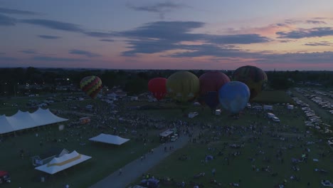 Luftaufnahme-Von-Heißluftballons,-Die-Sich-Für-Eine-Nächtliche-Flammenshow-Bei-Einem-Ballonfestival-Bei-Sonnenuntergang-Füllen,-Wie-Von-Einer-Drohne-Gesehen