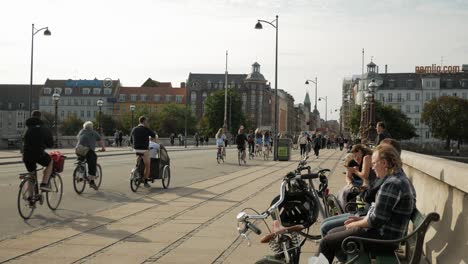 Street-of-Copenhagen,-people-riding-bicycle-and-sitting-on-benches