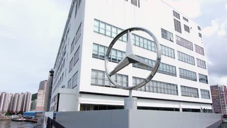 Large-Mercedes-Benz-sign-spinning-on-top-of-Hong-Kong-Mercedes-Benz-main-showroom-in-Chai-Wan-area,-Aerial-view