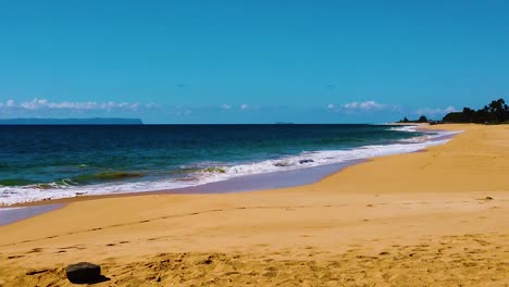 HD-Hawaii-Kauai-slow-motion-static-wide-shot-of-ocean-waves-washing-up-on-the-beach-along-bottom-and-right-frame-with-an-island-in-distance-in-left-frame-with-a-few-clouds-on-horizon-on-a-sunny-day