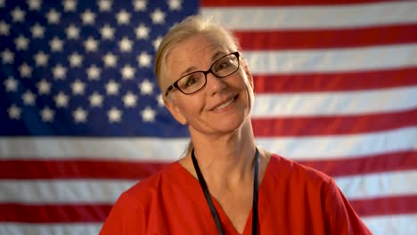 Medium-tight-portrait-of-a-healthcare-nurse-with-clipboard-looking-happy-and-relieved-walking-towards-camera-with-an-out-of-focus-American-flag