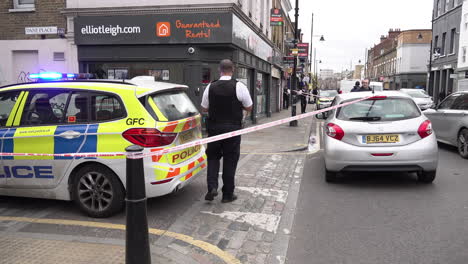 Police-officers-guard-a-cordon-in-a-suburban-high-street-marked-out-by-red-and-white-“Police-line-do-not-cross”-tape-at-the-scene-of-a-crime