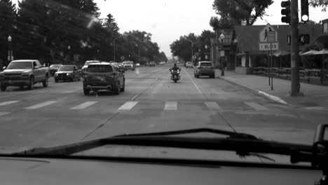 Black-and-white-clip-of-a-car-following-a-motorcycle-through-a-small-mountain-town-in-Wyoming,-US