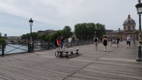Pont-Des-Arts-Brücke-Mit-Dem-Französischen-Institut-Und-Wenigen-Menschen,-Die-An-Sommertagen-In-Paris,-Frankreich,-Auf-Der-Holzterrasse-Spazieren,-Weite-Pfanne