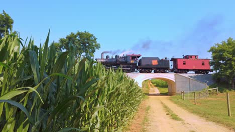 View-of-an-Approaching-Steam-Engine-Blowing-Smoke-and-Steam-Going-Over-a-small-Bridge-on-a-Sunny-Summer-Day