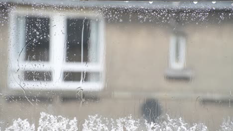 Close-up-of-melting-sleet-on-a-window-while-it-rains-outside