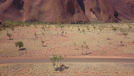 Die-Drohne,-Die-Einen-Weißen-Lieferwagen-Verfolgt,-Zeigt-Im-Hintergrund-Den-Spektakulären-Uluru-Ayres-Felsen