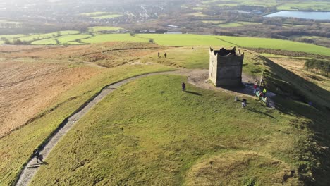 Above-runners-on-summit-of-Rivington-tower-Lancashire-reservoir-countryside-aerial-view-pull-away-orbit-left