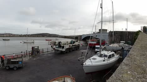 Hydraulic-crane-vehicle-lifting-fishing-boat-vessel-into-Conwy-harbour-water-waterfront-timelapse