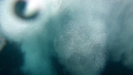 Man-dives-forward-from-the-side-deck-of-a-yacht-close-to-the-island-shore,-Dive-underwater-follow-shot