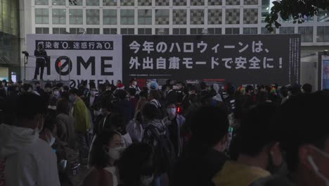 Riesiges-Banner,-Das-Die-Menschen-Auffordert,-In-Der-Halloween-Nacht-Zu-Hause-Zu-Bleiben,-Hängt-Vor-Dem-Bahnhof-Shibuya---Coronavirus-Pandemie---Zeitlupe