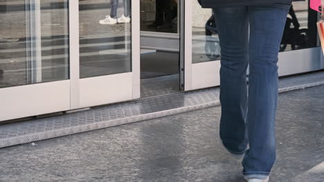 Woman-In-Jeans-With-Paper-Bag-Walks-Inside-The-Store-Door-To-Shop-In-Monza,-Italy---Static-Shot,-Slow-Motion