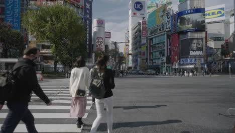 Während-Der-Pandemie-Gehen-Menschen-An-Einem-Sonnigen-Tag-Mit-Einem-Einkaufszentrum-Im-Hintergrund-In-Tokio,-Japan,-Am-Shibuya-Kreuz-Entlang