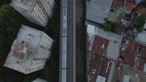 Aerial-top-down-following-train-moving-between-Belgrano-neighborhood-buildings-and-houses,-Buenos-Aires,-Argentina