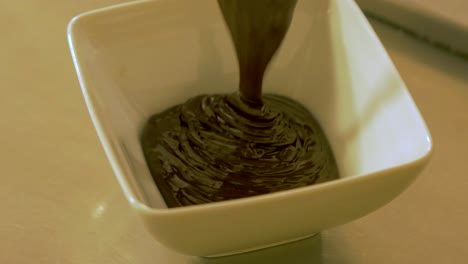 Verter-Chocolate-Oscuro-Derretido-En-La-Pequeña-Papilla-Blanca,-Primer-Plano-De-Mano