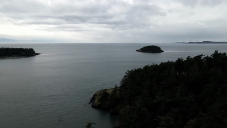 Pulling-back-over-the-rugged-shoreline,-dark-storm-clouds-on-the-Puget-Sound-horizon,-aerial