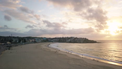 People-Strolling-At-Bondi-Beach-In-Sydney,-NSW-On-A-Beautiful-Sunrise---aerial-drone