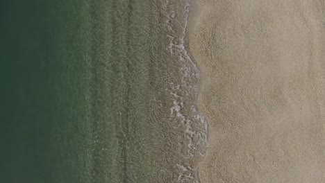 Kleine-Wellen-Plätschern-An-Einem-Goldenen-Sandstrand,-Während-Die-Kamera-Nach-Oben-Geneigt-Ist-Und-Den-Blick-Auf-Die-Küste-Freigibt