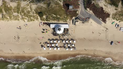 AERIAL:-Top-View-Descending-Shot-of-White-Tents-on-a-Sandy-Nida-Beach-with-Waving-Flags