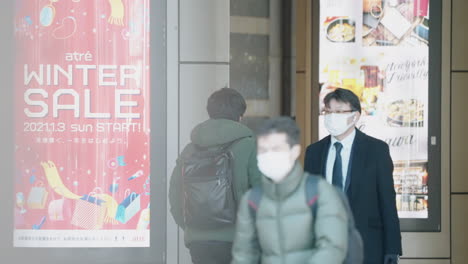 Covid-19-Neue-Variante-Der-Sicherheitsmaßnahme-–-Menschen,-Die-Während-Der-Pandemie-Den-Bahnhof-Shinagawa-Betreten-Und-Verlassen,-Tragen-Gesichtsmasken-Mit-Werbung-An-Der-Wand-In-Tokio,-Japan