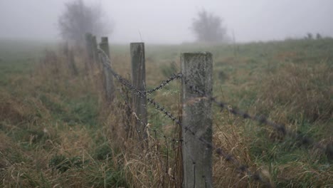 Barbed-wire-fence-on-farmland-on-a-foggy-misty-day-wide-shot
