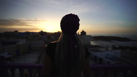 Chica-Caucásica-Viendo-La-Hermosa-Puesta-De-Sol-Desde-El-Balcón-Del-Hotel-En-Essaouira,-Marruecos