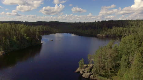 Very-beautiful-aerial-video-of-a-Finnish-lake-and-forests-in-summer-time,-two-swans-swimming-in-the-end