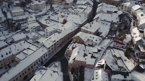Flying-above-Christian-Church-and-rooftops-covered-by-snow-in-Mining-town-Banska-Stiavnica,-Aerial-shot