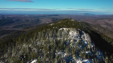 Aerial-orbit-around-the-rocky-outcrop-at-the-peak-of-a-snow-dusted-mountain-in-Maine