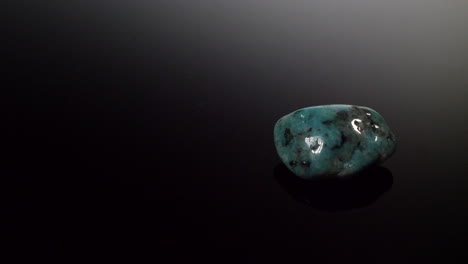 Ein-Blau-türkisfarbener-Mineralstein,-Isoliert-Auf-Einem-Schwarzen,-Reflektierenden-Hintergrund