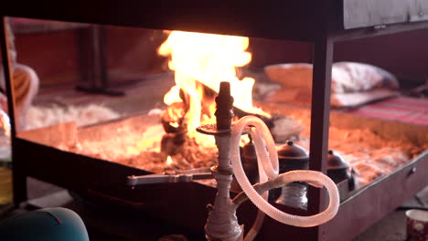 A-Person-Sitting-Next-to-a-Fireplace-and-Heating-a-Stove-With-an-Iron-Fire-Poker,-Slowmotion-100-Frames-Per-Second