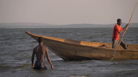 Toma-En-Cámara-Lenta-De-Un-Pescador-Africano-Empujando-Su-Canoa-De-Madera-Tradicional-Pasó-Nadadores-En-El-Lago-Victoria