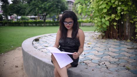 A-hot-Asian-girl-is-studying-under-a-tree-inside-University-college-campus-ground,-reading-a-book